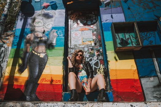 Stylish woman in biker jacket posing against a vibrant graffiti wall in city.