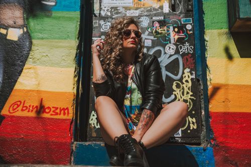 Free Fashionable woman in a leather jacket poses against a vibrant mural in a city setting. Stock Photo