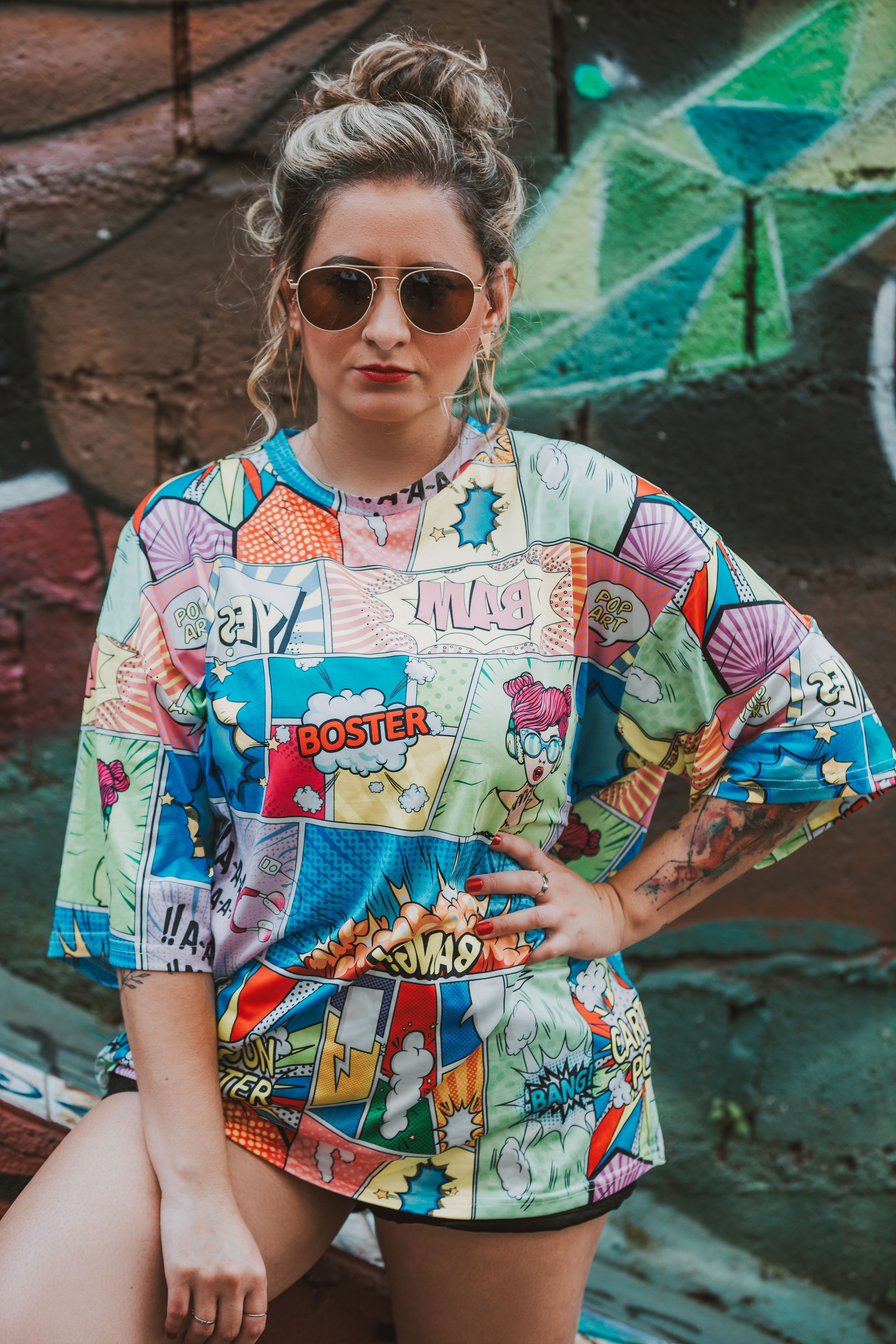 Mulher estilosa em camiseta colorida com estampa de quadrinhos contra uma parede de grafite vibrante.