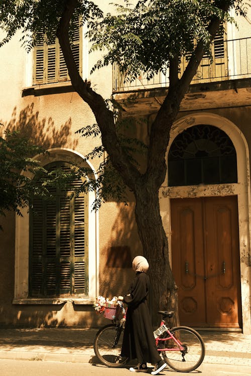 Woman in Hijab Walking with Bicycle near Tree on Street