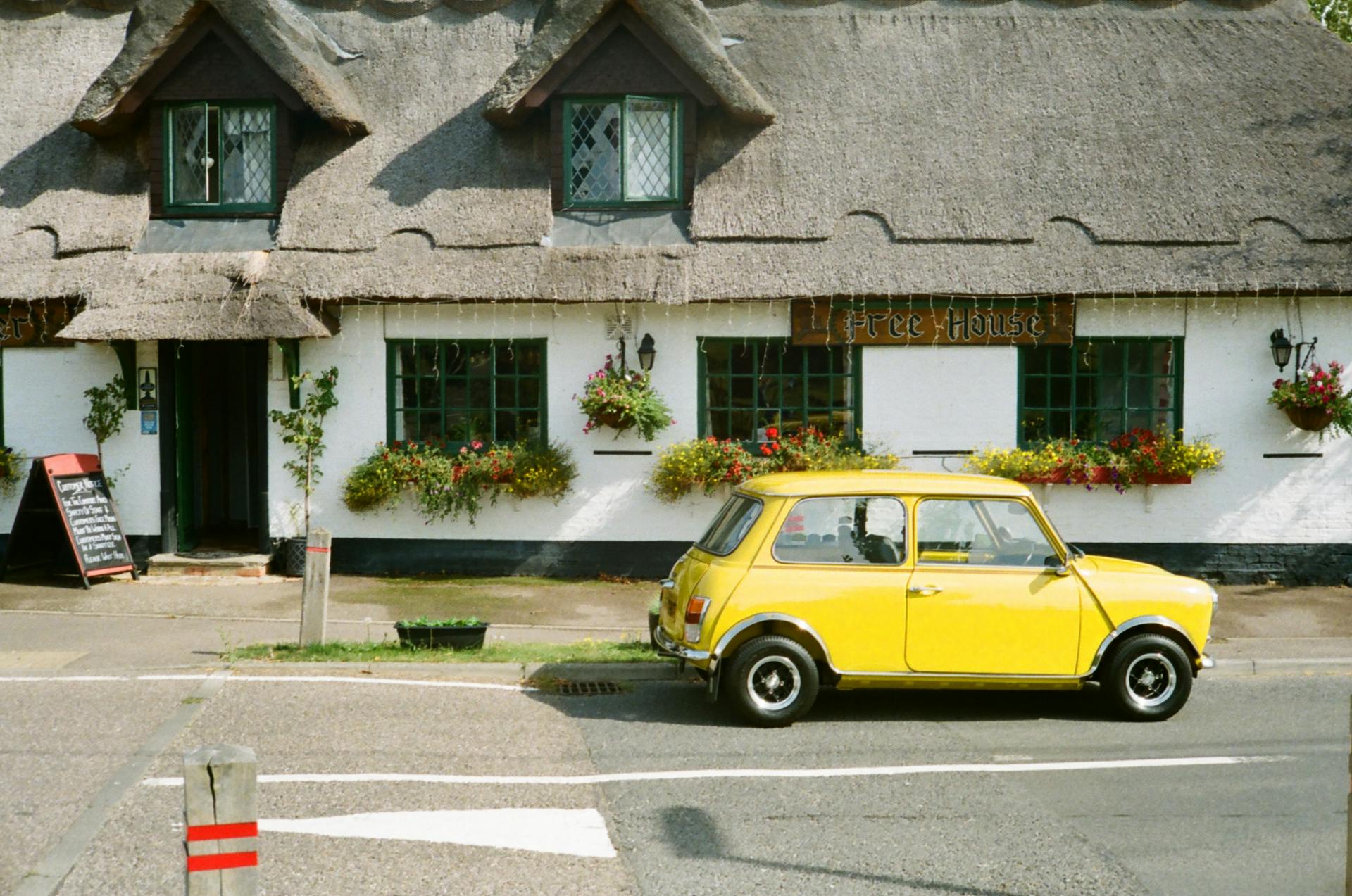 Charming scene of a classic yellow car parked on a UK street beside a rustic thatched-roof cottage.