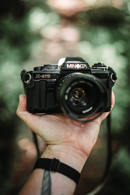 Hand holding a classic Minolta X-570 film camera outdoors, showcasing vintage photography gear.