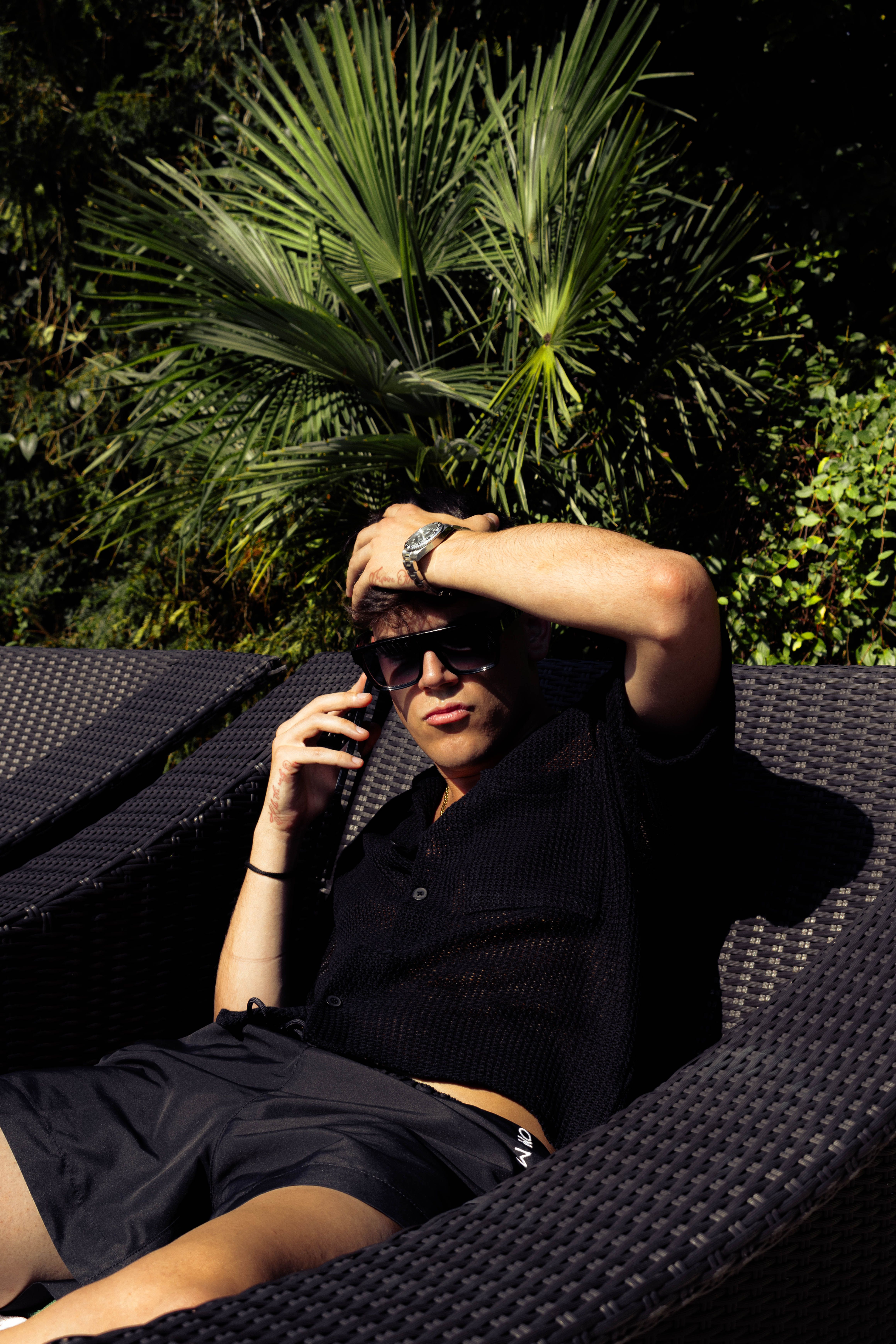 Man lounging under tropical sun with palm leaves, enjoying a vacation vibe.