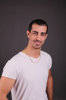 A confident man smiling casually against a dark studio background.