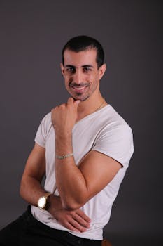 Portrait of a confident young man in a casual outfit against a dark background, smiling at the camera.
