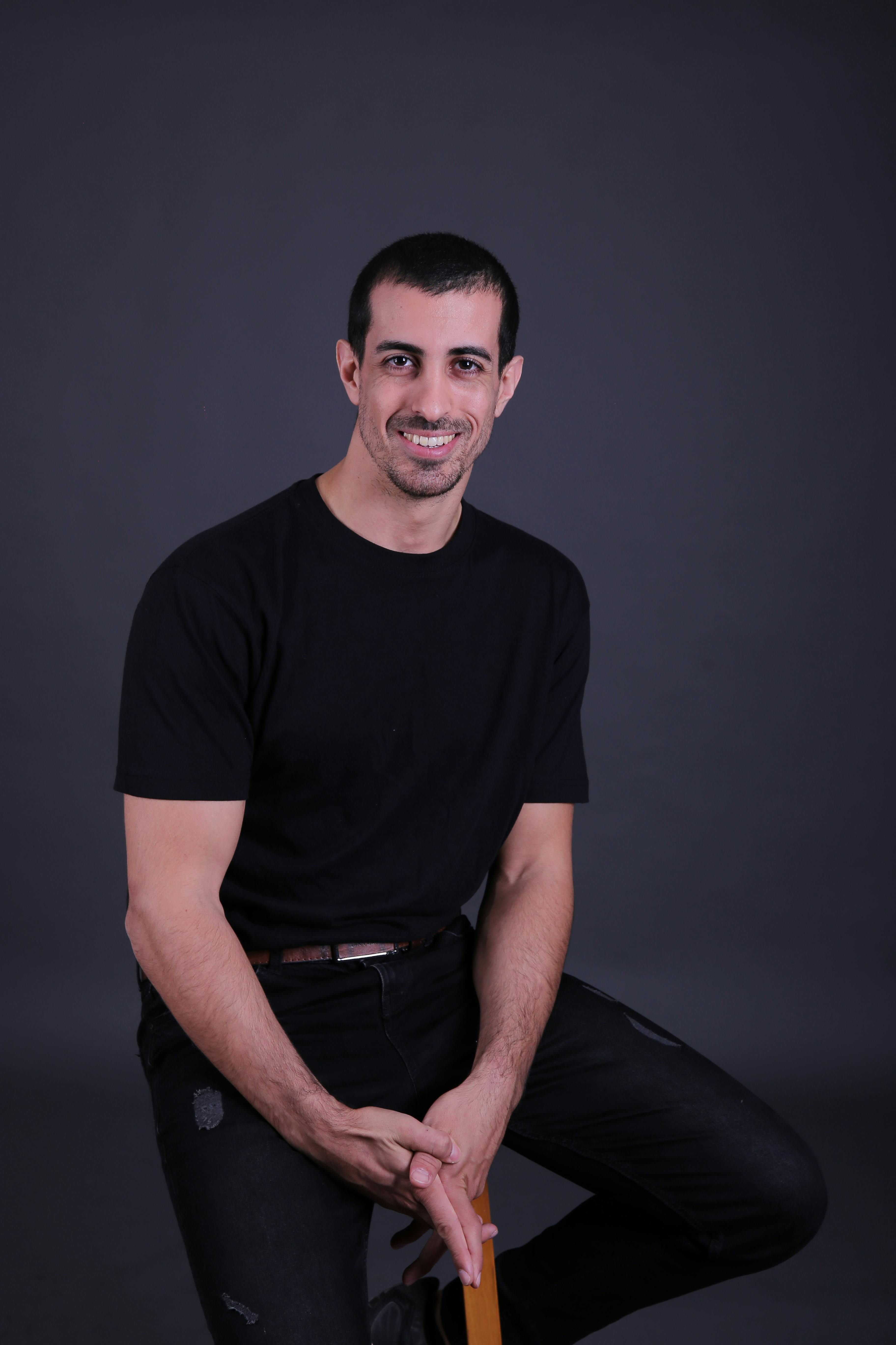 Professional studio portrait of a man in casual black attire, smiling confidently.