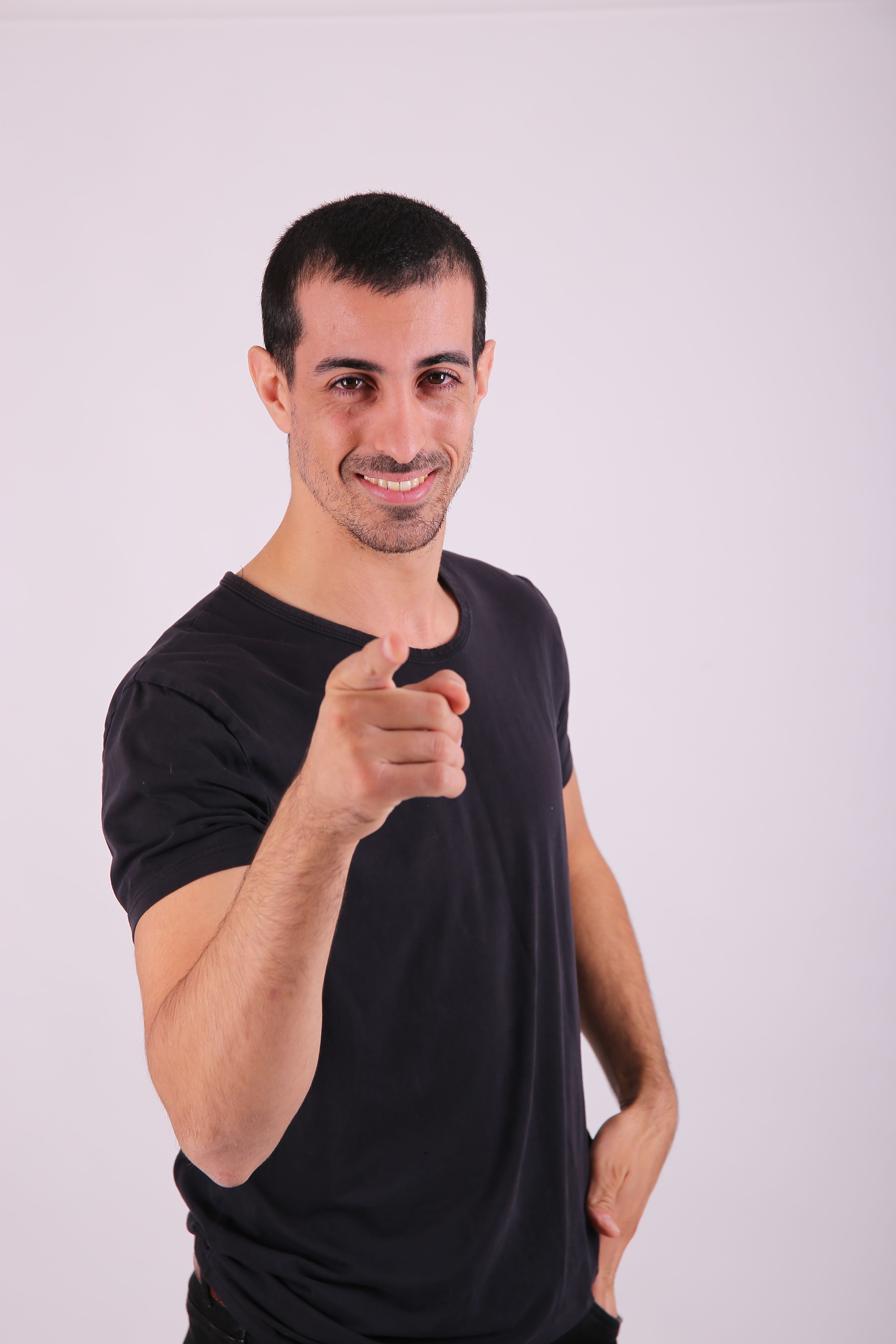 Young man in casual attire confidently pointing at the camera with a smile.