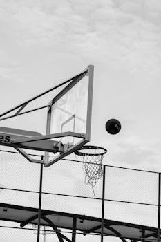 Monochrome image of a basketball hoop and ball in an urban setting, showcasing an outdoor sports scene.