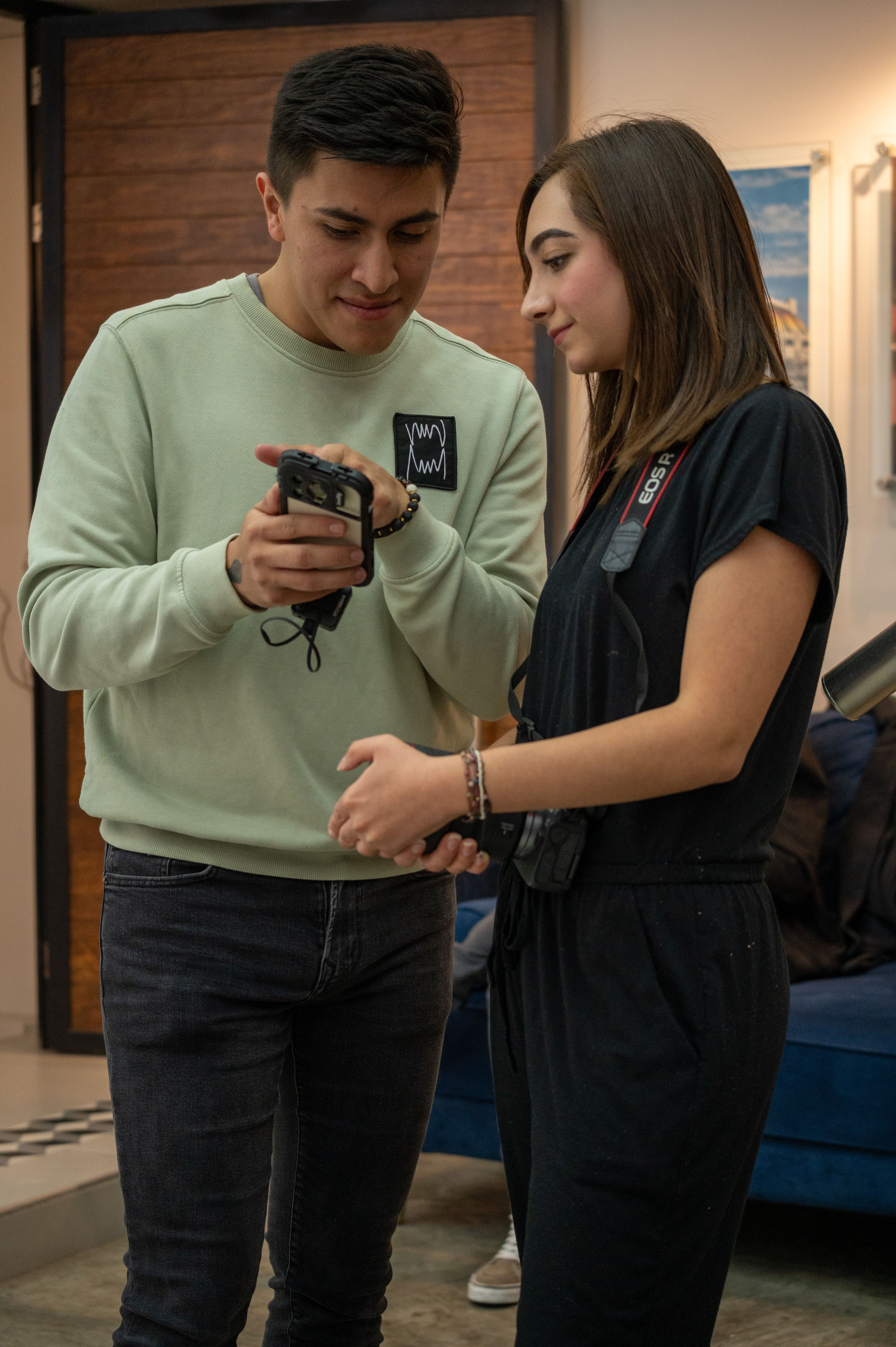 A young couple engaging with a smartphone in a cozy indoor setting, wearing casual attire.