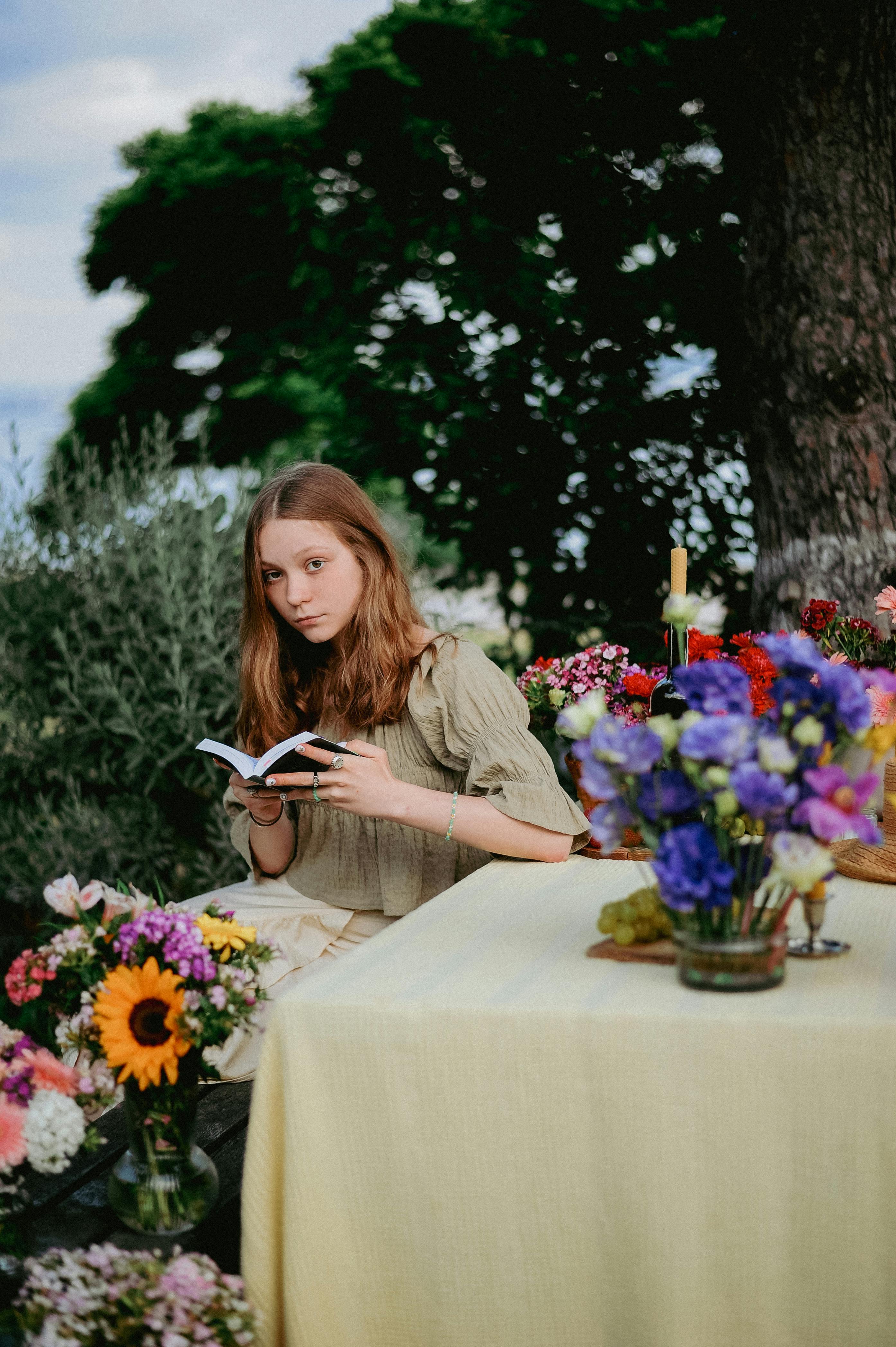 Teen girl enjoys reading outdoors surrounded by vibrant summer flowers.
