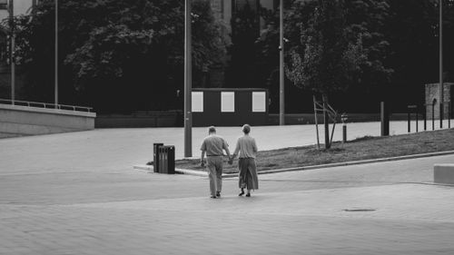 Free A senior couple walking hand in hand on a paved path in a city park. Stock Photo