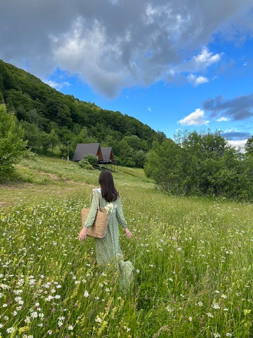 Woman in Green Dress Walking on Meadow with Flowers
