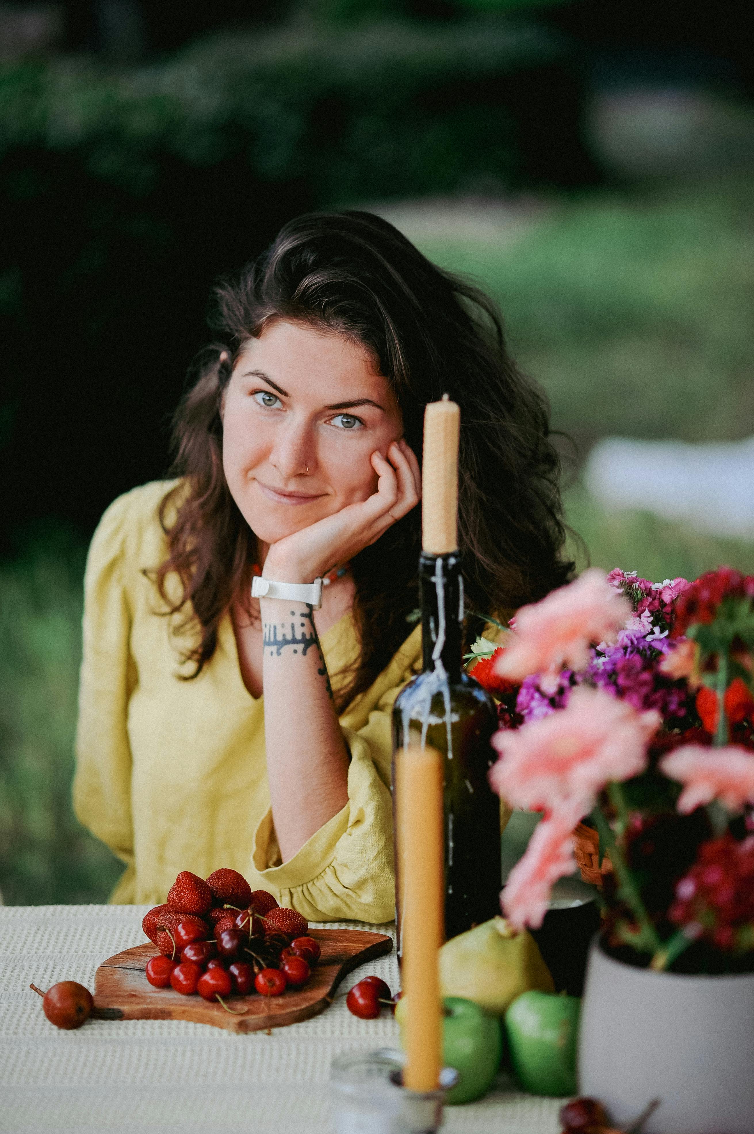 Charming portrait of a woman in a garden setting with fruits and flowers on a table.