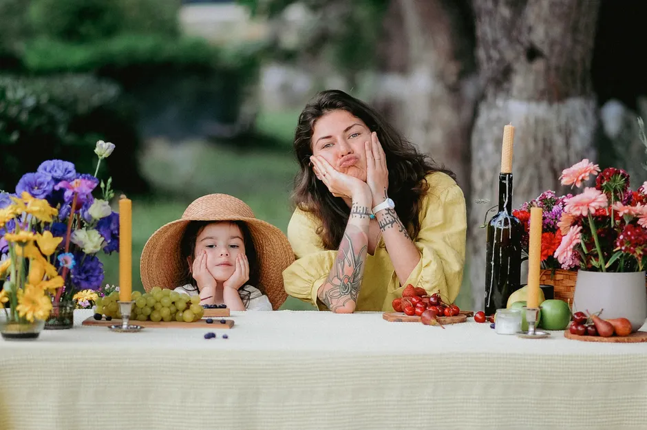 Mother and daughter with a small visible tattoo sharing a playful outdoor picnic moment