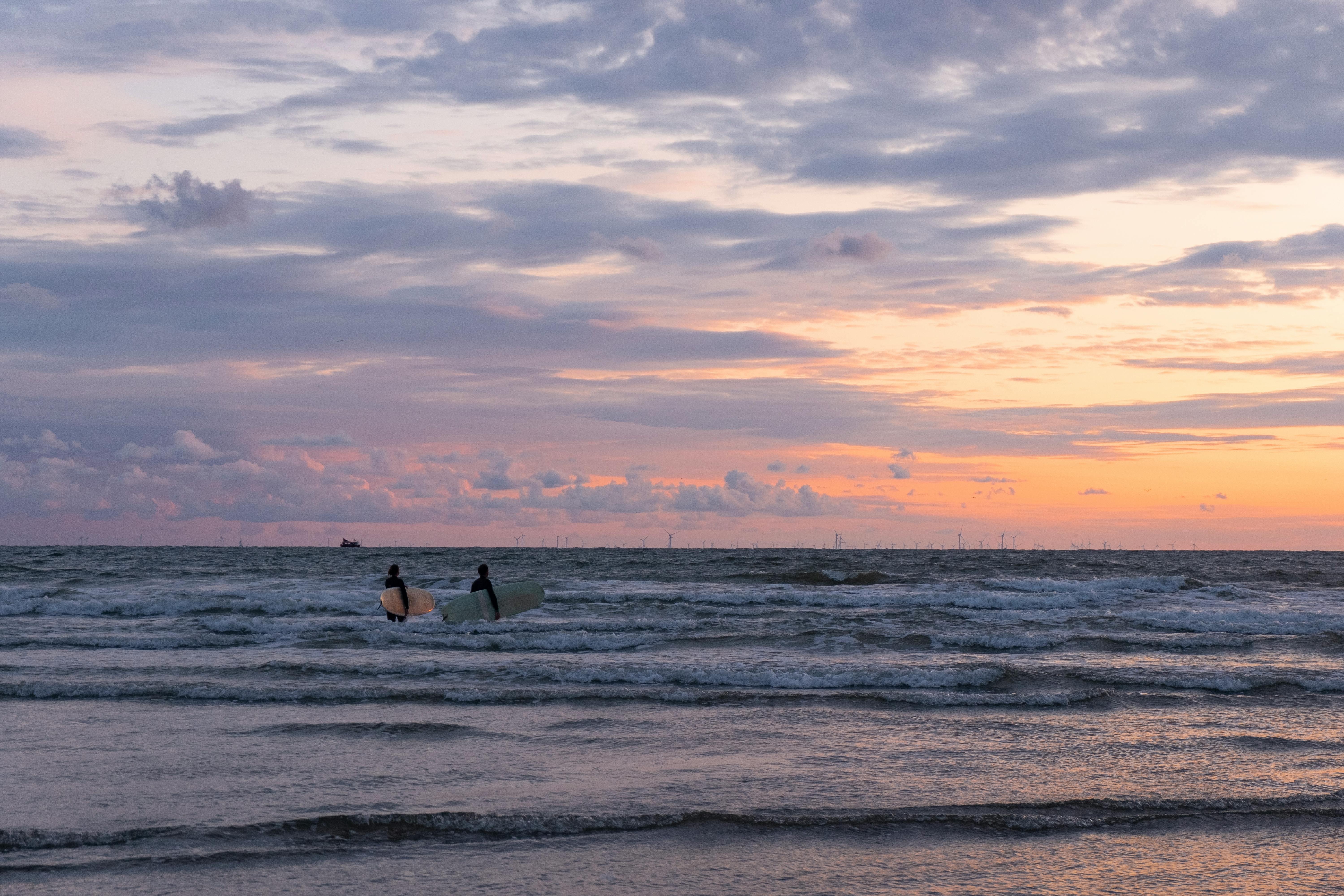 Two surfers walking into the sea at sunset on IJmuiden beach, Netherlands.