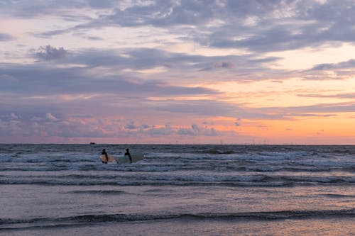 People with Surfboards Walking in Sea on Sunset