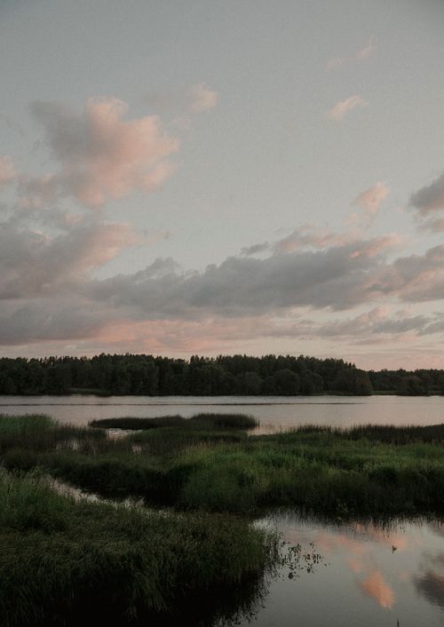 Free Peaceful evening view of a tranquil lake surrounded by lush greenery and a colorful sky. Stock Photo