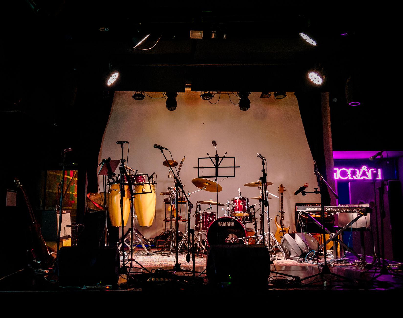 Imagen de archivo: Un escenario vacío dispuesto con instrumentos musicales listos para una actuación en vivo en un lugar poco iluminado.