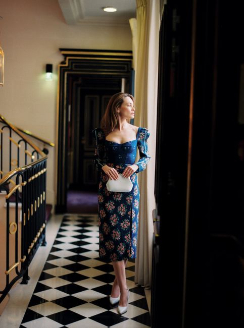 Chic woman in a floral dress gazing outside with elegance indoors.