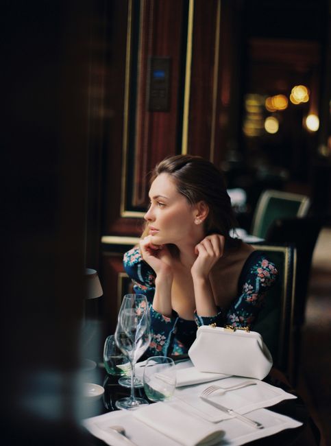 Elegant woman in floral dress sitting at a fine dining restaurant table with a leather purse.