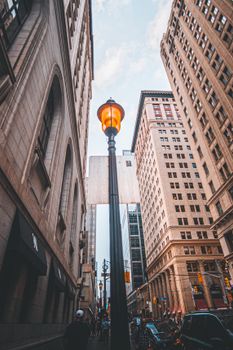 Low angle shot of a city street with skyscrapers and a glowing street lamp.