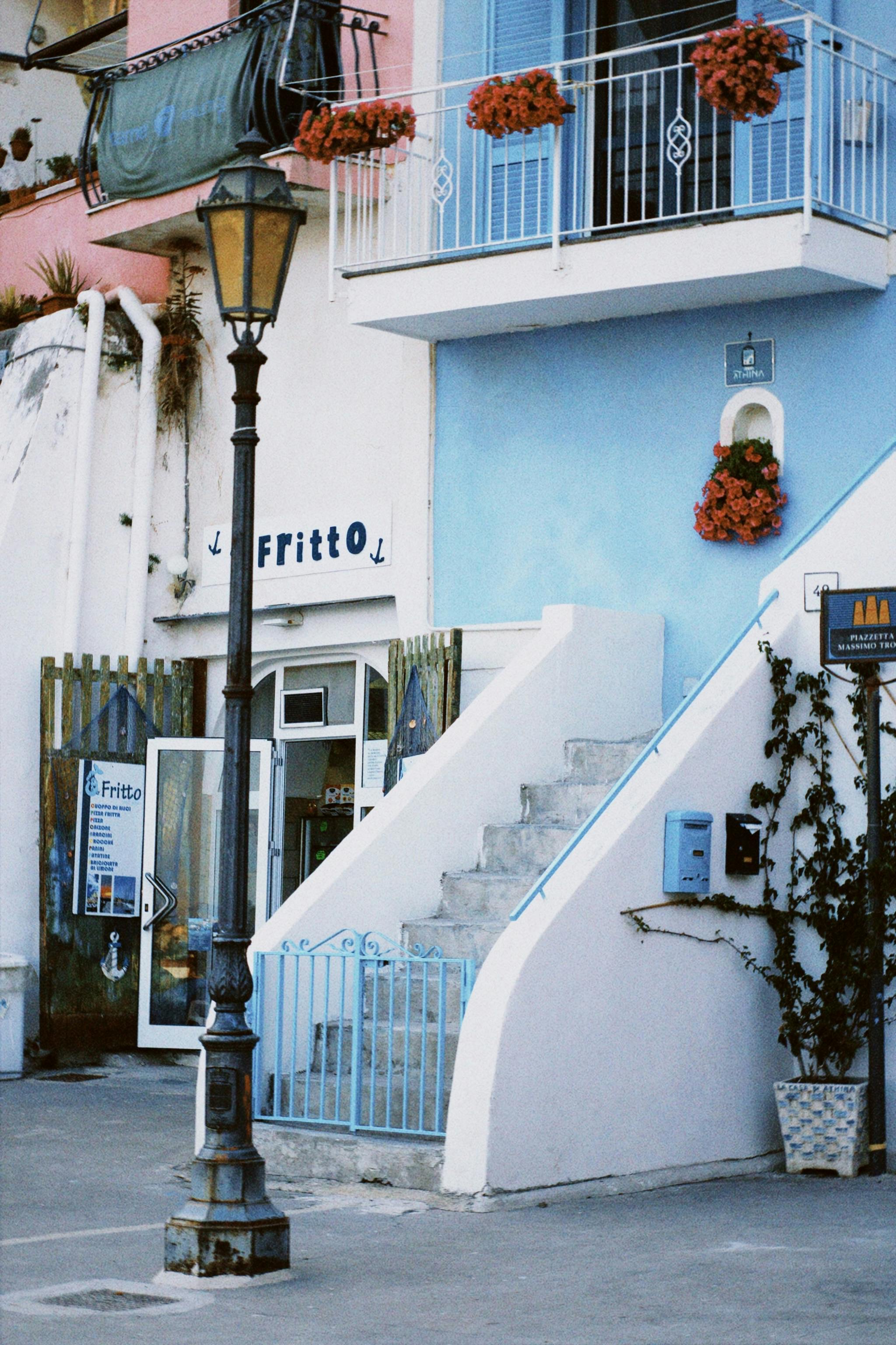 A picturesque blue building with a balcony and flowers in an urban setting.