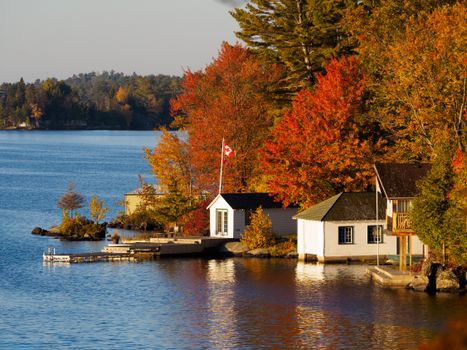Tranquil lake scene with autumn foliage and Canadian flag by cozy houses.
