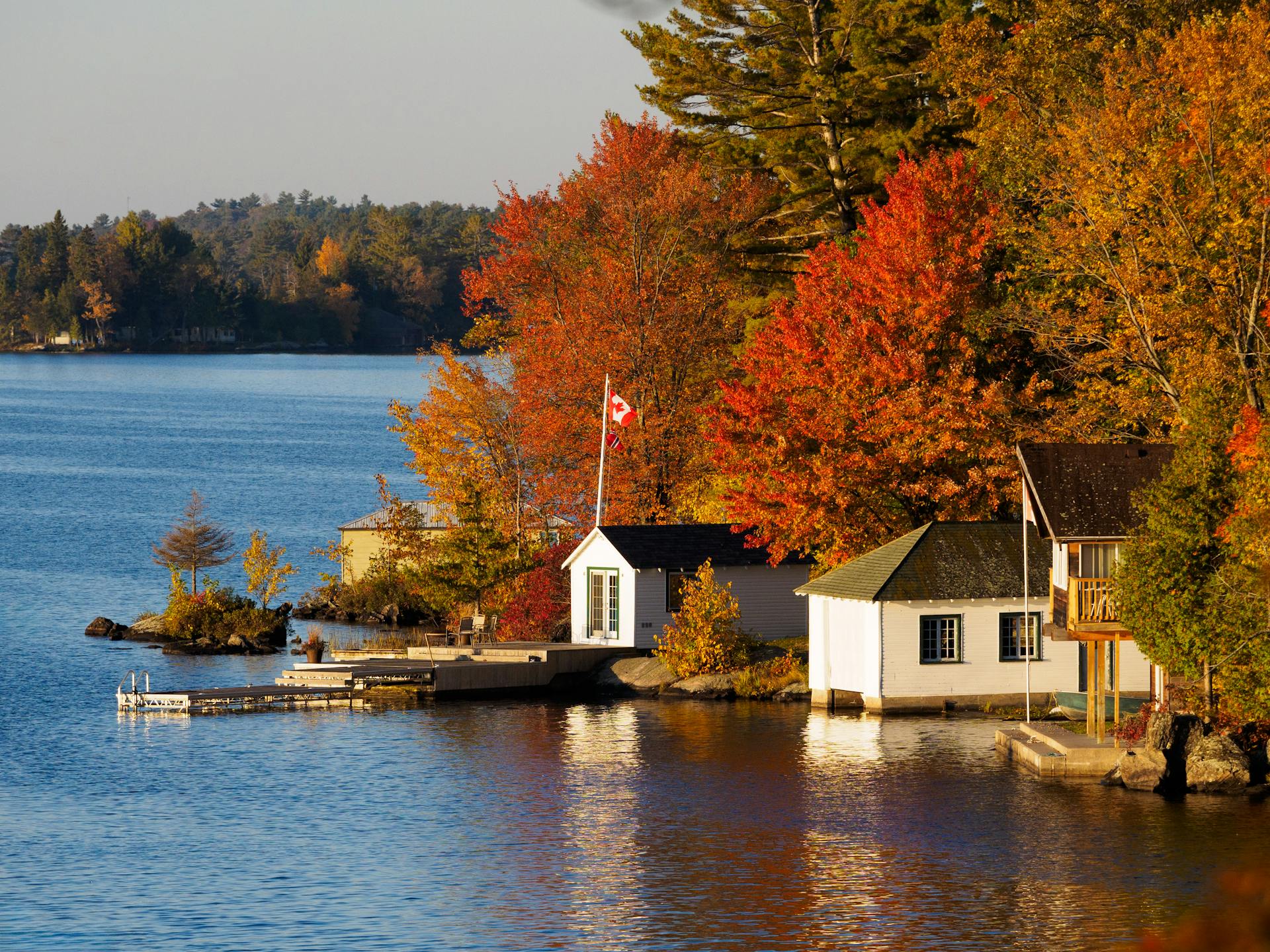 Canadian Flag Flying above House Built on Lake Shore under Autumn Trees