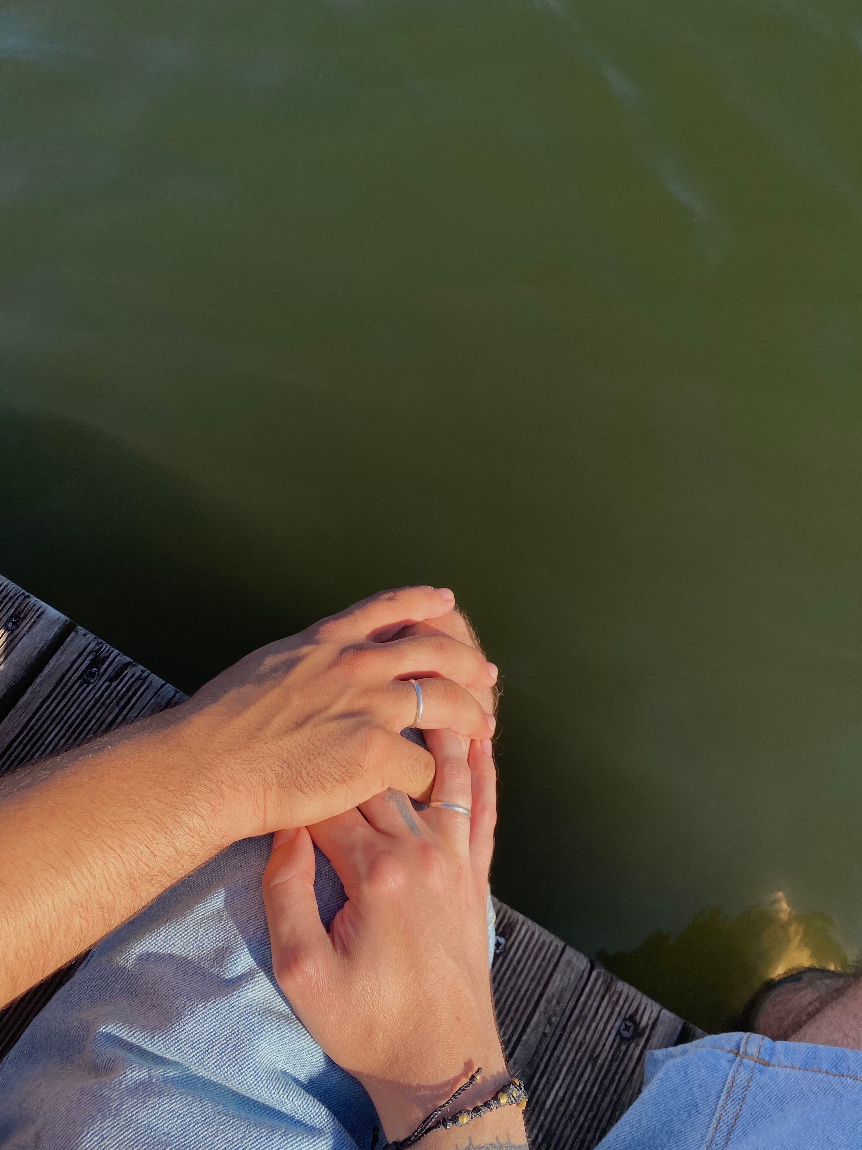 Close-up of couple holding hands on a dock by the water, symbolizing love and connection.