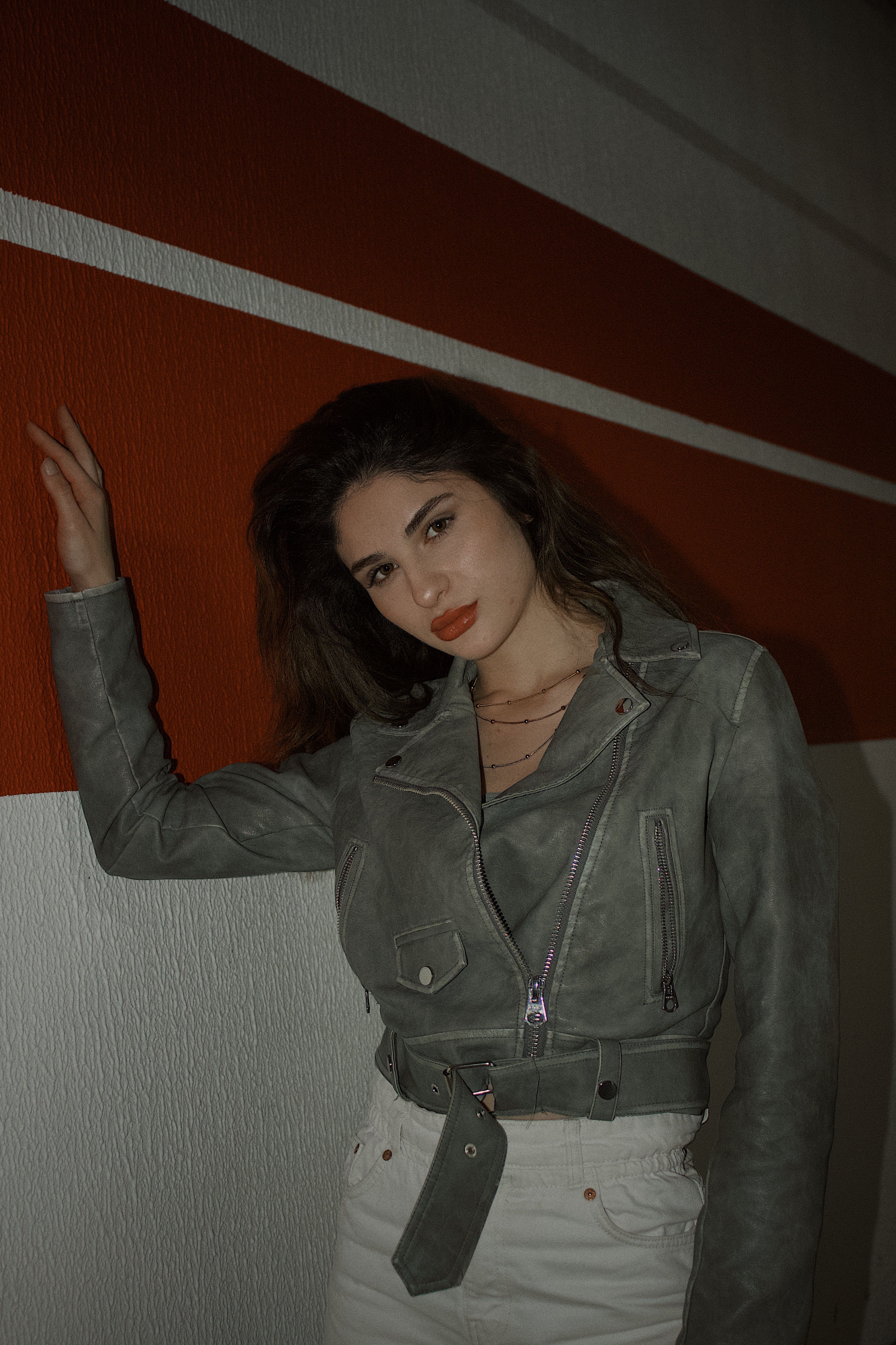In a modern outdoor setting, a woman poses in a leather jacket against a bold striped wall.