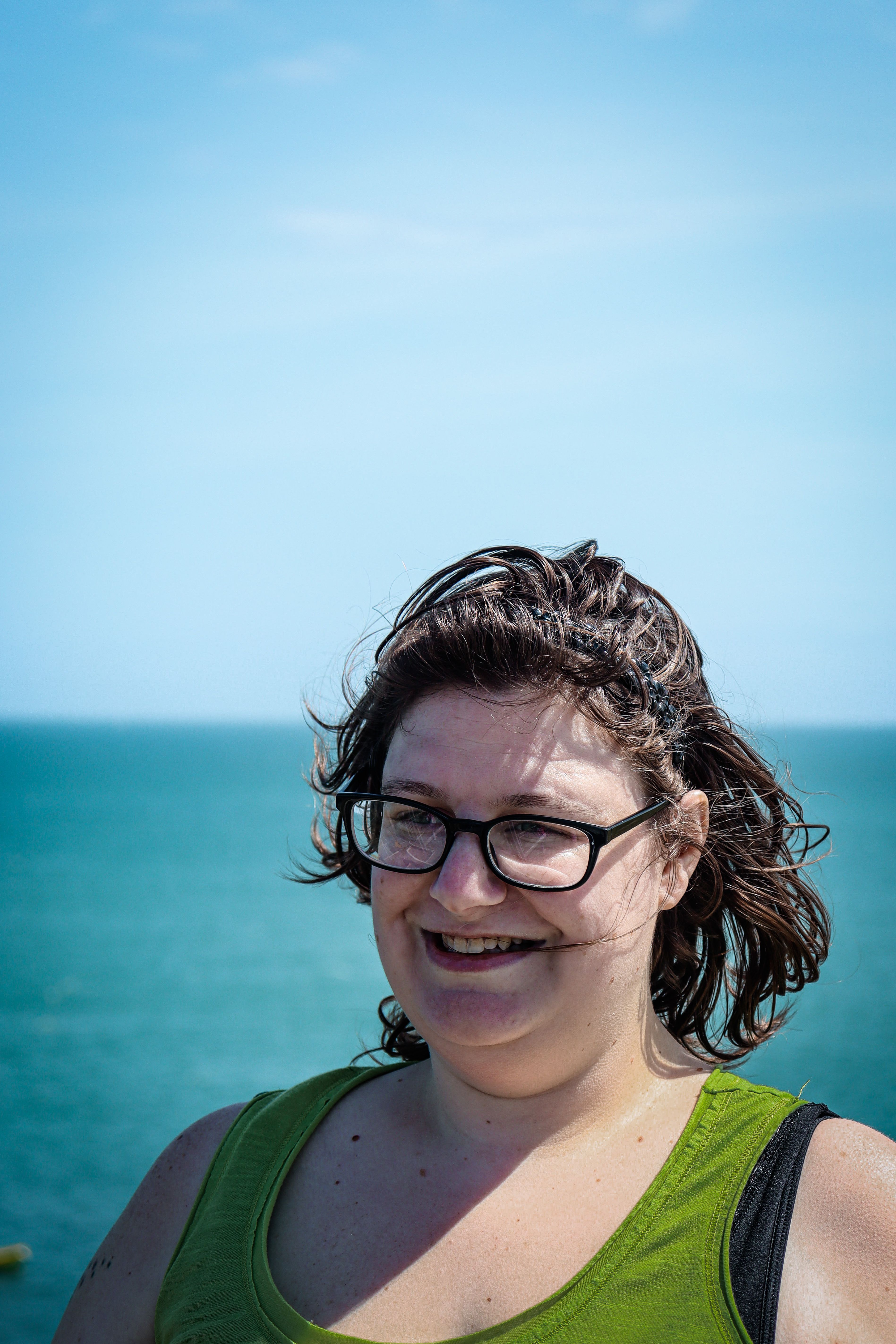 Portrait of a smiling woman wearing glasses at the seaside on a sunny day.
