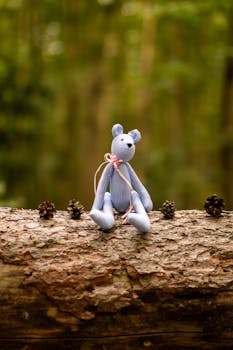 Adorable teddy bear seated on a log in the forest surrounded by pine cones.