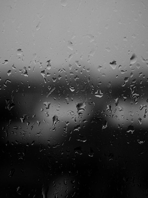 Free Close-up view of rain droplets on a window, creating a moody atmosphere in black and white. Stock Photo