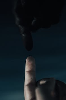 在黑暗背景下，两个手指几乎相触的戏剧性特写，传达出紧张与期待