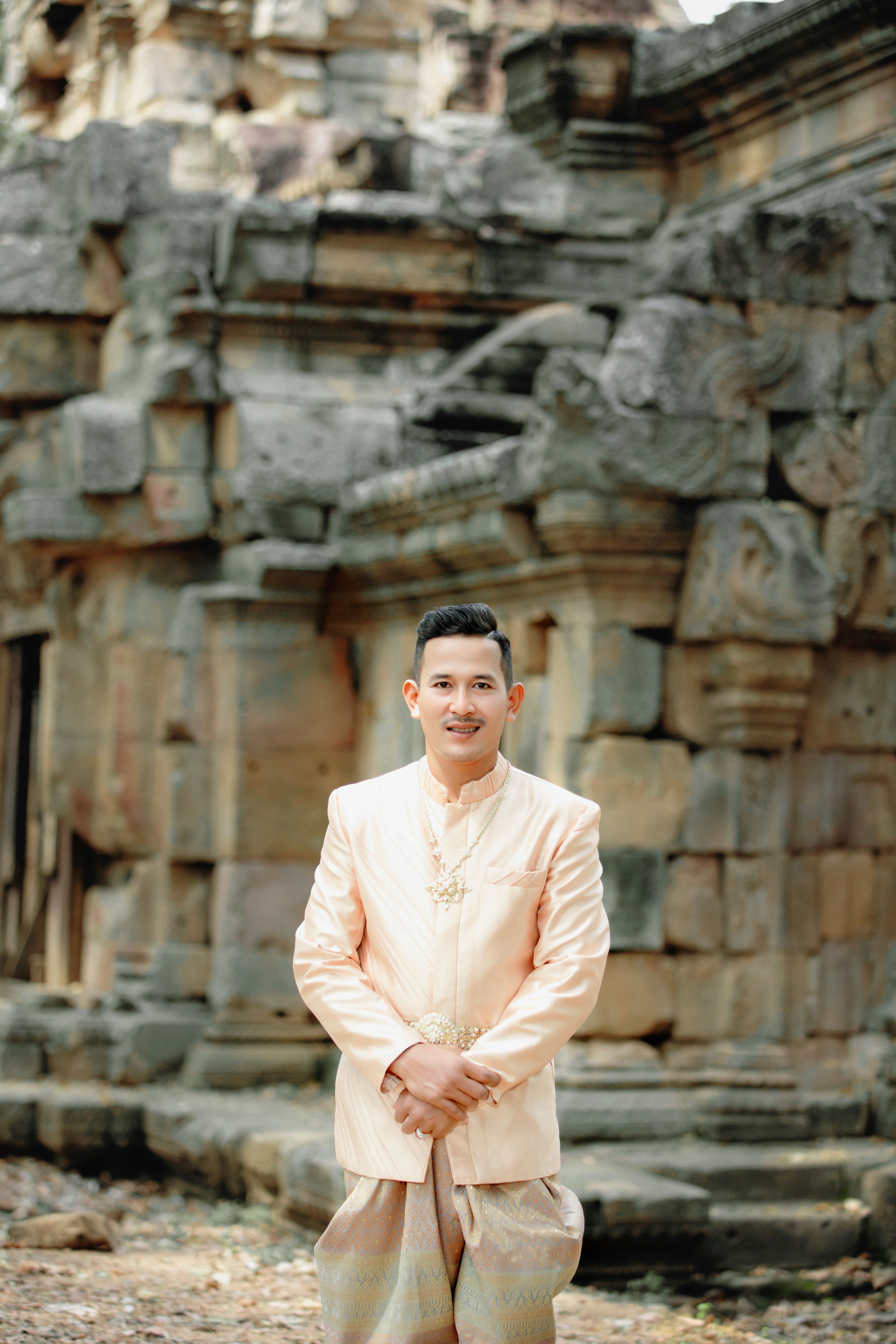 Traditional portrait of a man in elegant clothing in front of an ancient stone temple.