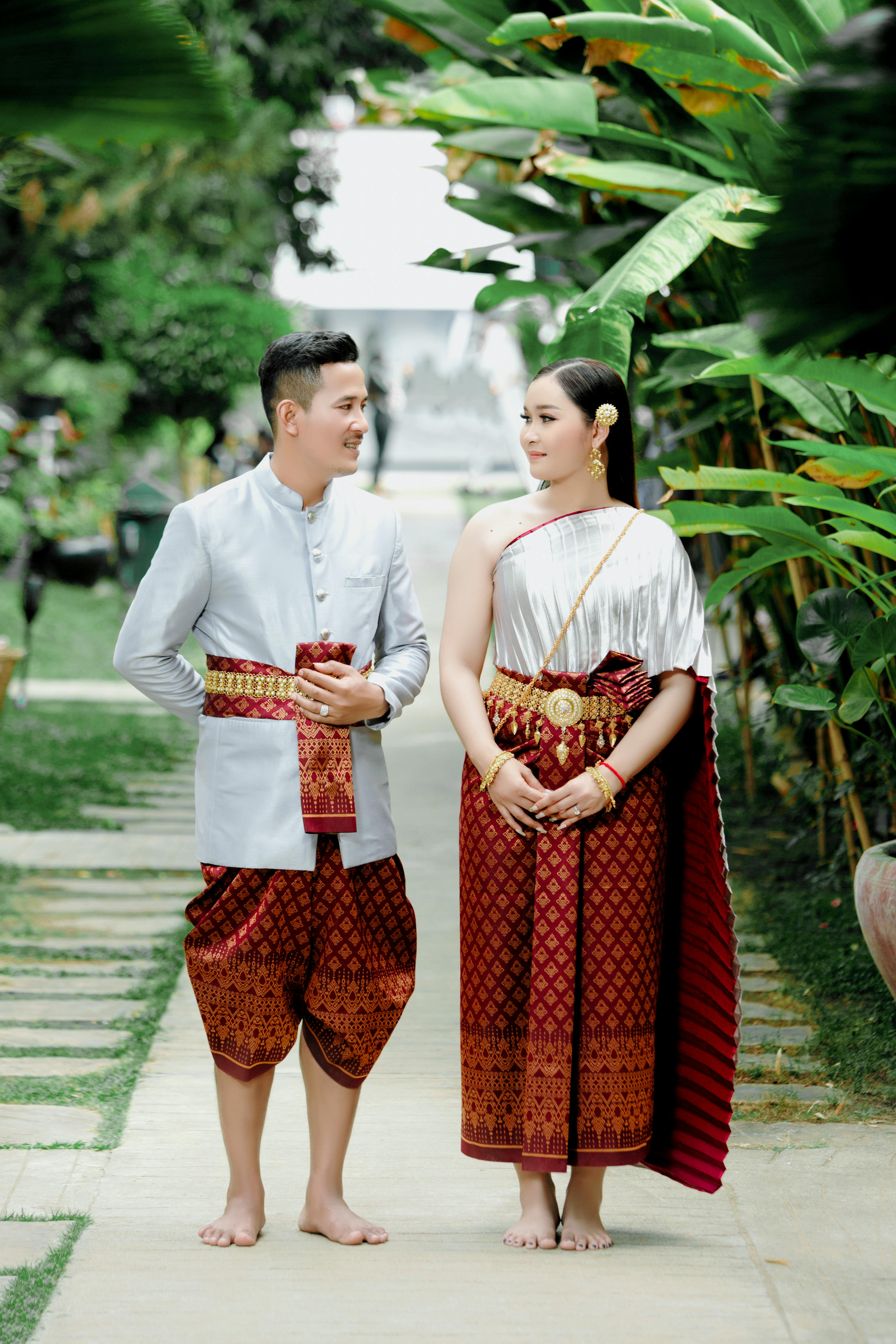 A couple stands together in traditional Thai clothing, showcasing cultural elegance.