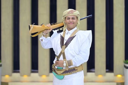 A Yemeni man proudly wears traditional attire with a rifle, showcasing cultural heritage.