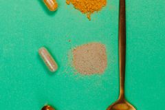 Top view of a golden spoon with capsules and powders on a vibrant green surface, representing supplements.