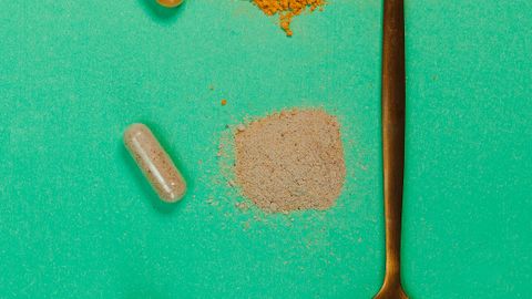 Top view of a golden spoon with capsules and powders on a vibrant green surface, representing supplements.