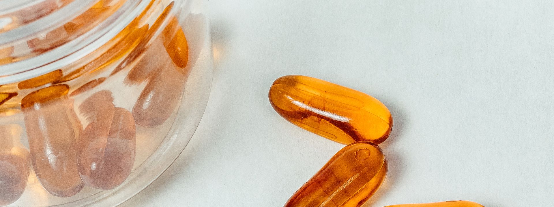 Transparent yellow softgel capsules beside an open bottle on a white background