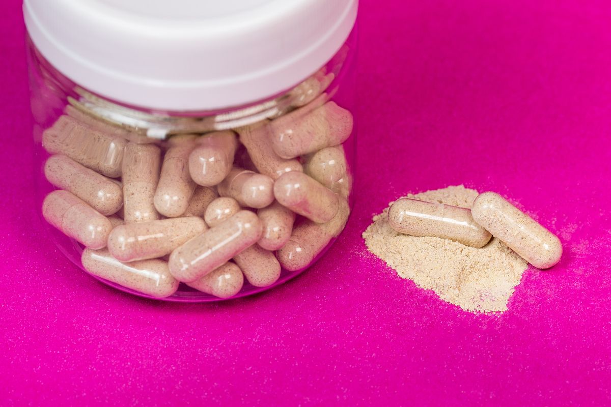 Pote de vidro com capsulas e po de suplemento sobre fundo rosa vibrante