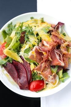 Colorful salad with prosciutto, avocado, beets, and fresh greens, perfect for a healthy lunch.