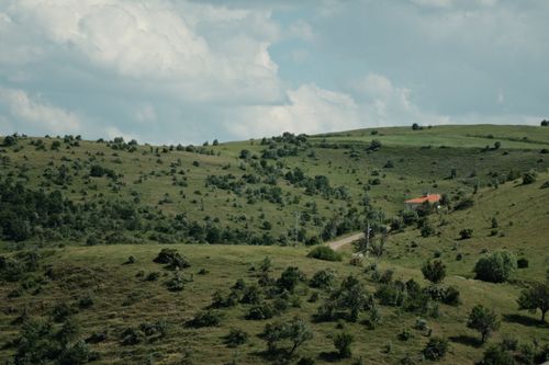 Free Beautiful aerial view of rolling green hills and a country house under a cloudy sky Stock Photo