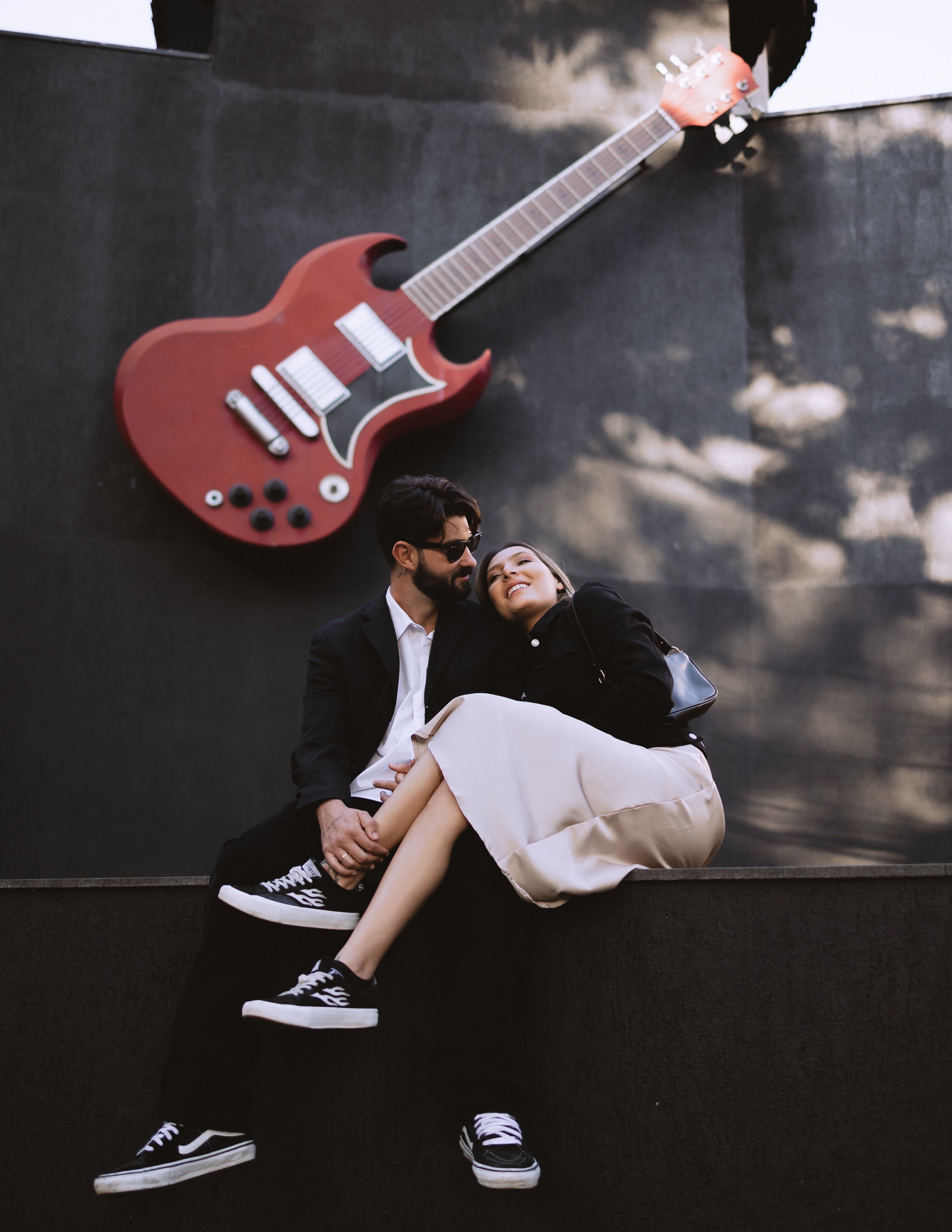 Young couple embracing under a large guitar sculpture, outdoors.