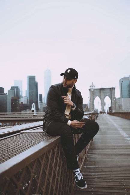 Fashionable man sitting on Brooklyn Bridge with NYC skyline in the background.