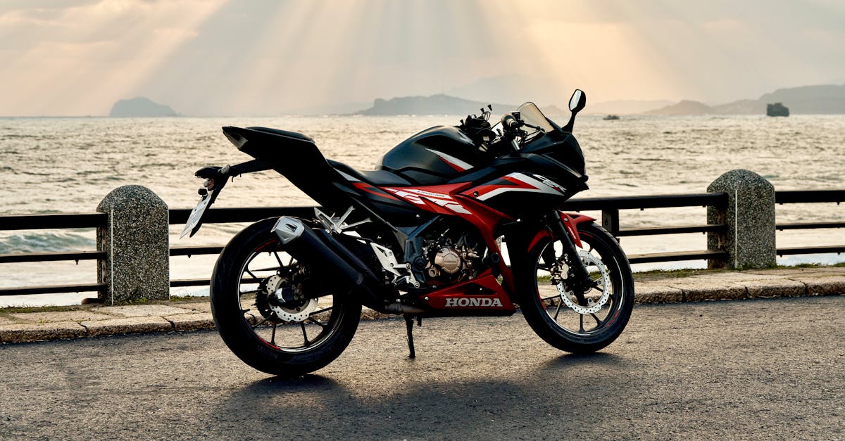 A sleek black and red motorcycle parked by the ocean as the sun sets in the background.