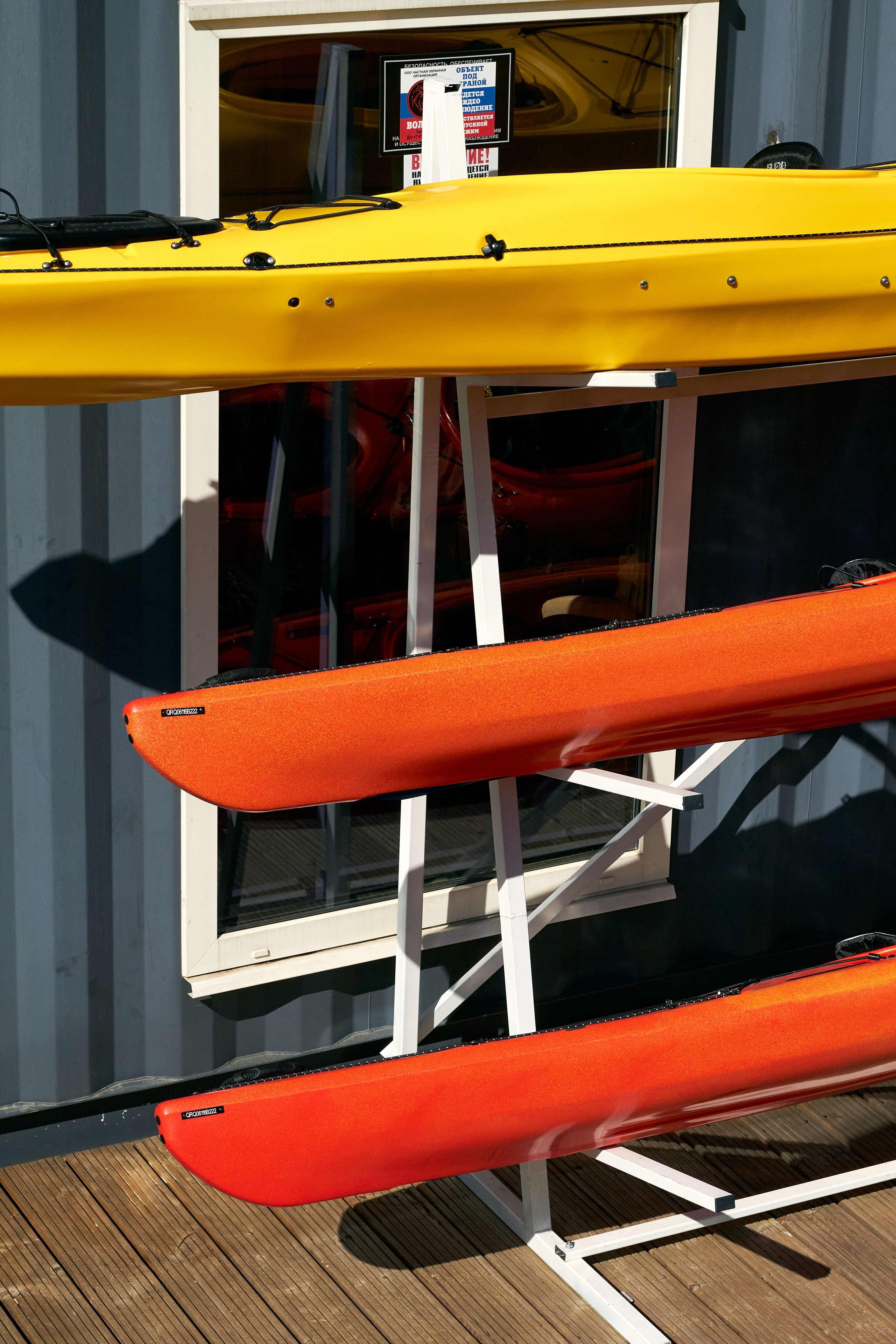 Bright yellow and orange kayaks stacked outside a warehouse in summer sunlight.