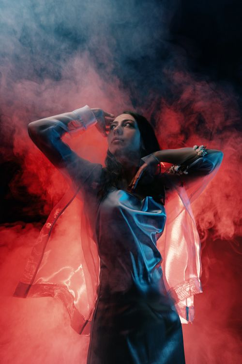 Free Stylish woman in a transparent coat posing in red and blue smoke. Stock Photo
