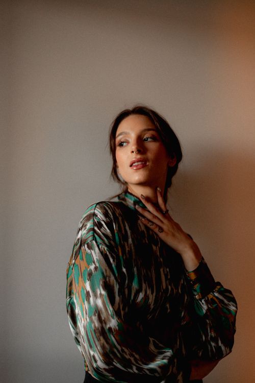 Free Elegant woman in floral-patterned blouse posing indoors with hand on neck. Stock Photo
