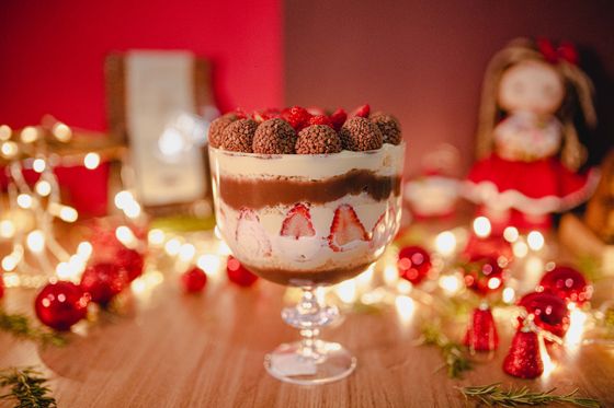 Footed glass trifle with strawberry halves, cream and chocolate layers topped with chocolate truffles